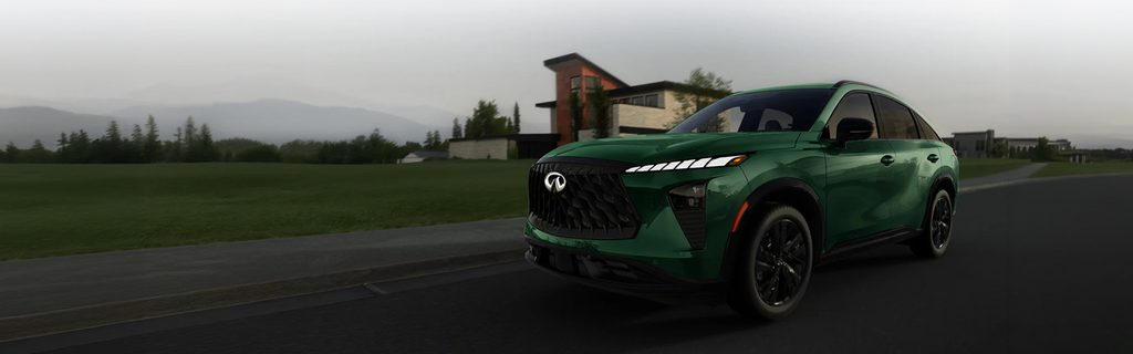 Green INFINITI QX60 SUV driving down street with mountains in background
